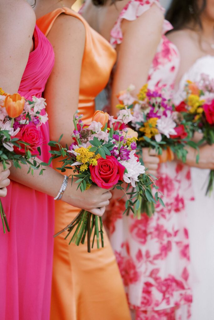 bridesmaids wearing pinkn orange and pink floral dresses, holding their bouquet at The Springs Event Venue Weatherford