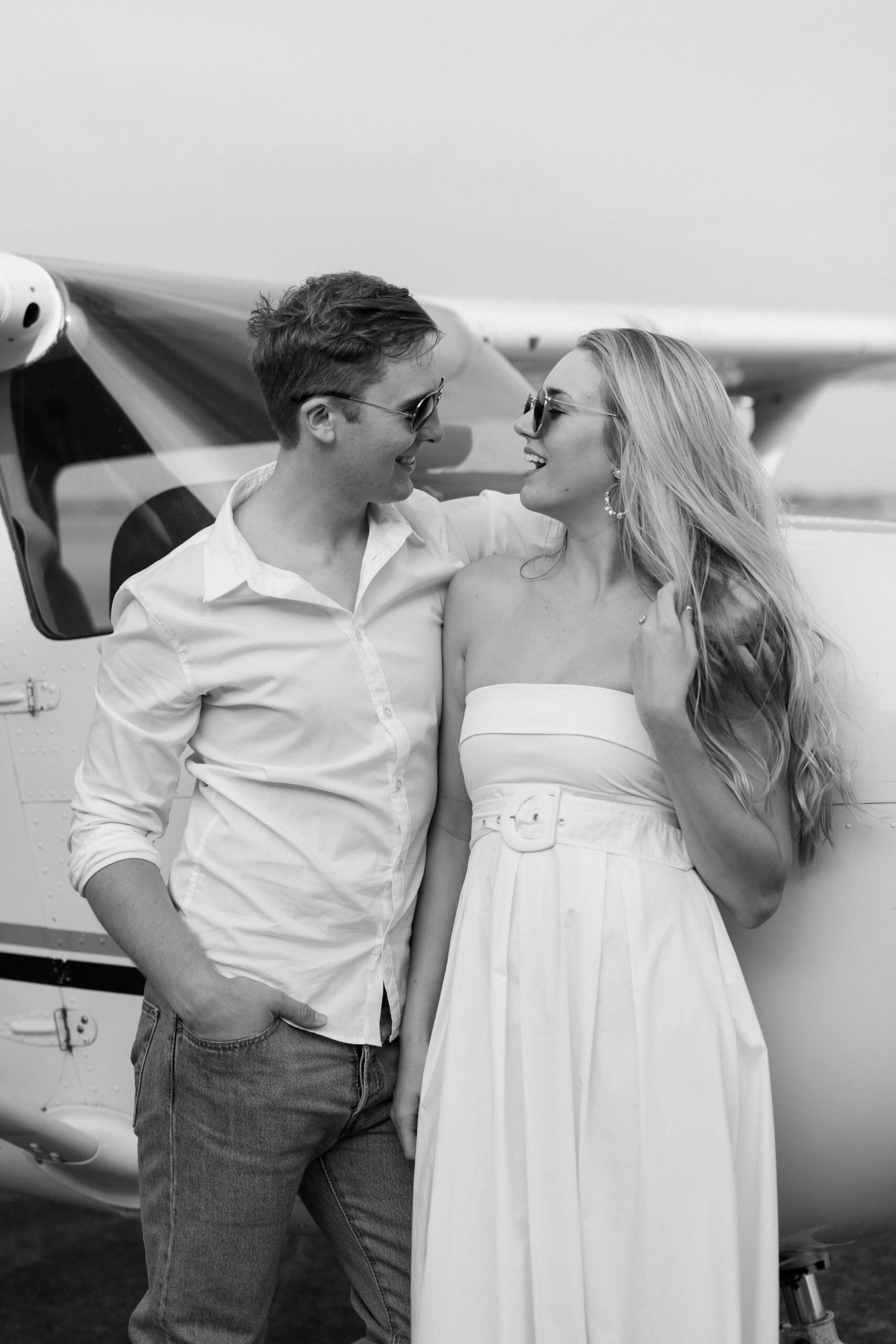 couple looking at each other wearing aviator glasses for their Airplane Engagement Session in Dallas-Fort Worth