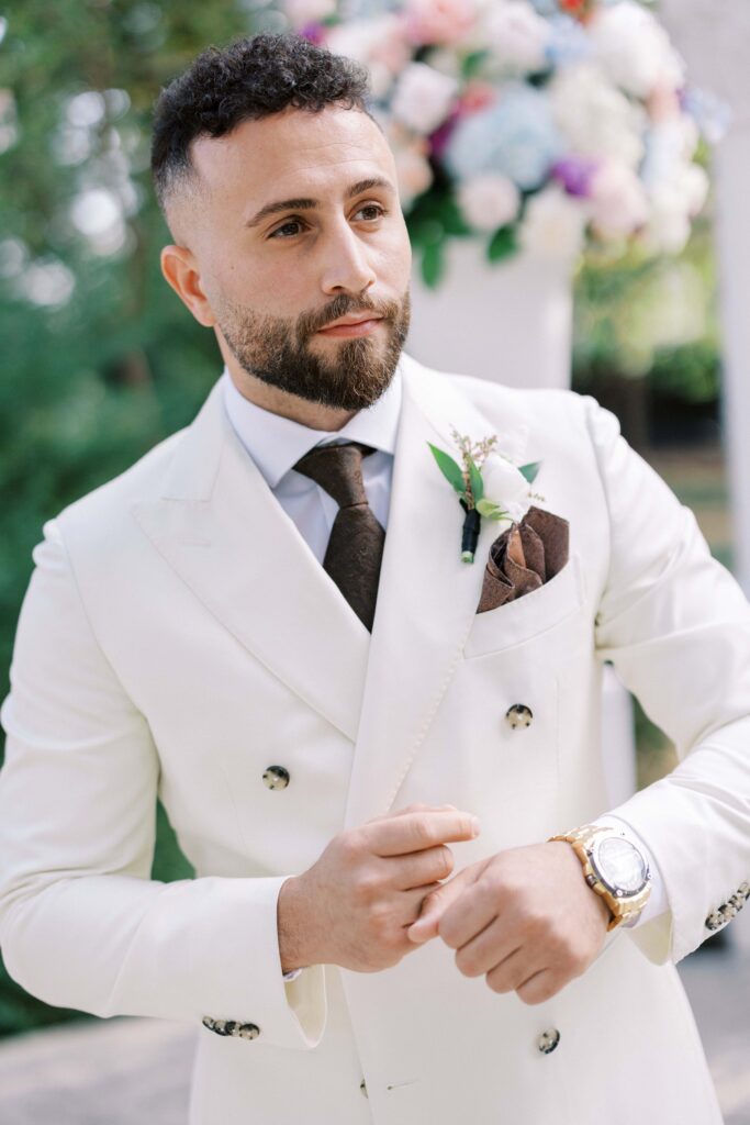 groom looking away wearing a white suit at his brighton abbey wedding