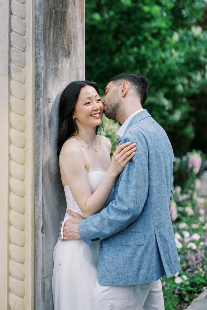 Alessandro kissing Rita on the cheek during their engagement photos at the Dallas Arboretum