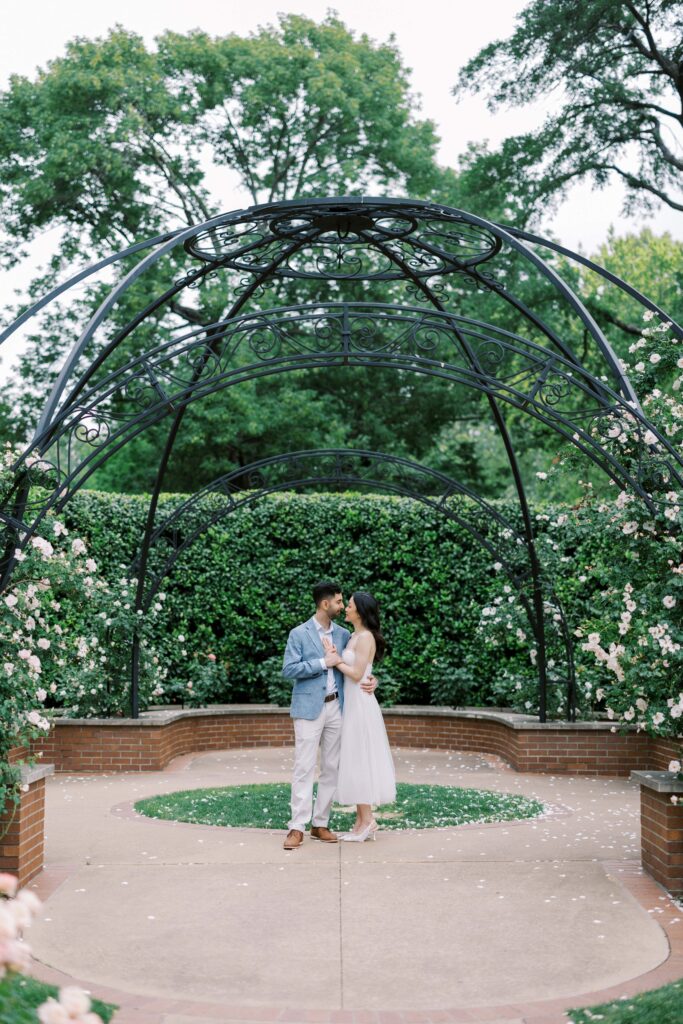 Rita and Alessandro in the rose garden holding each other for their engagement photos at the Dallas Arboretum