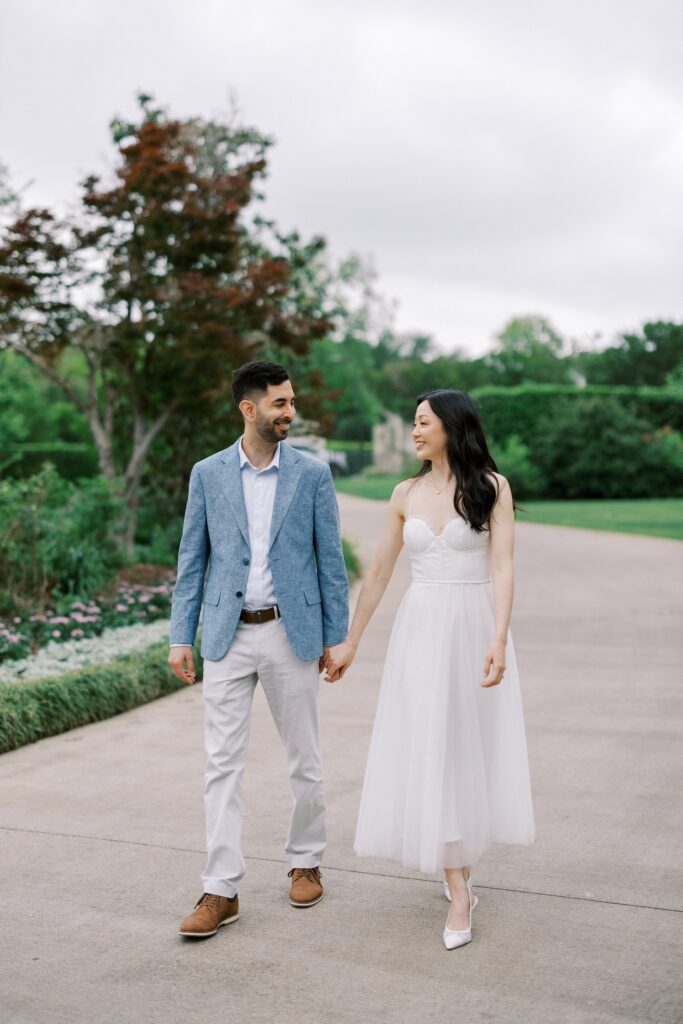 couple walking holding hands during their engagement photos at the Dallas Arboretum