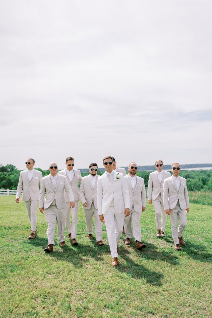 groomsmen walking towards the camera with sunglasses wearing white suits for this Lakeview Hills Wedding
