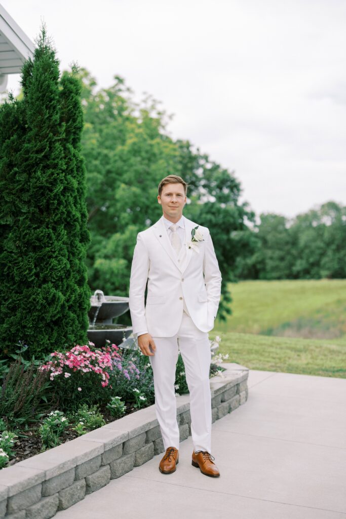 groom with one hand in the pocket in his white suit at his Lakeview Hills Wedding