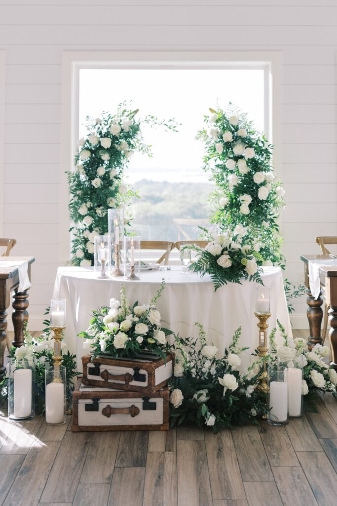 sweetheart table with luggages and all white flowers and floral arch in the back for this Lakeview Hills Wedding
