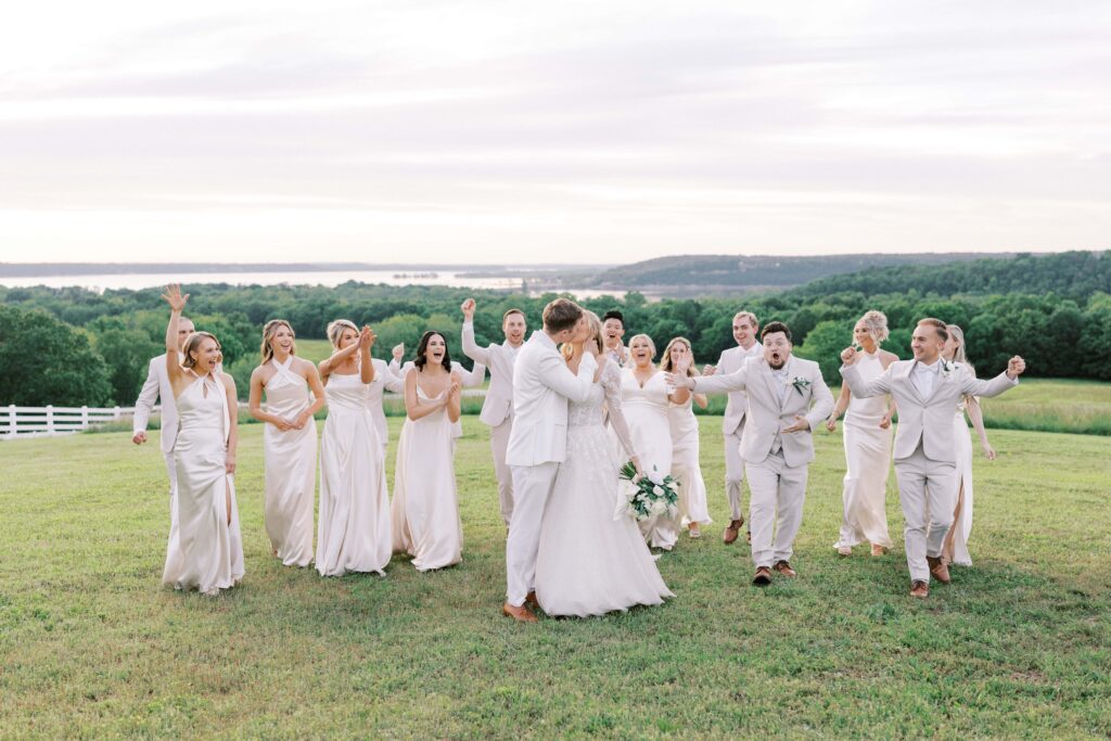bride and groom kissing while the bridal party cheers them on in the back at their Lakeview Hills Wedding
